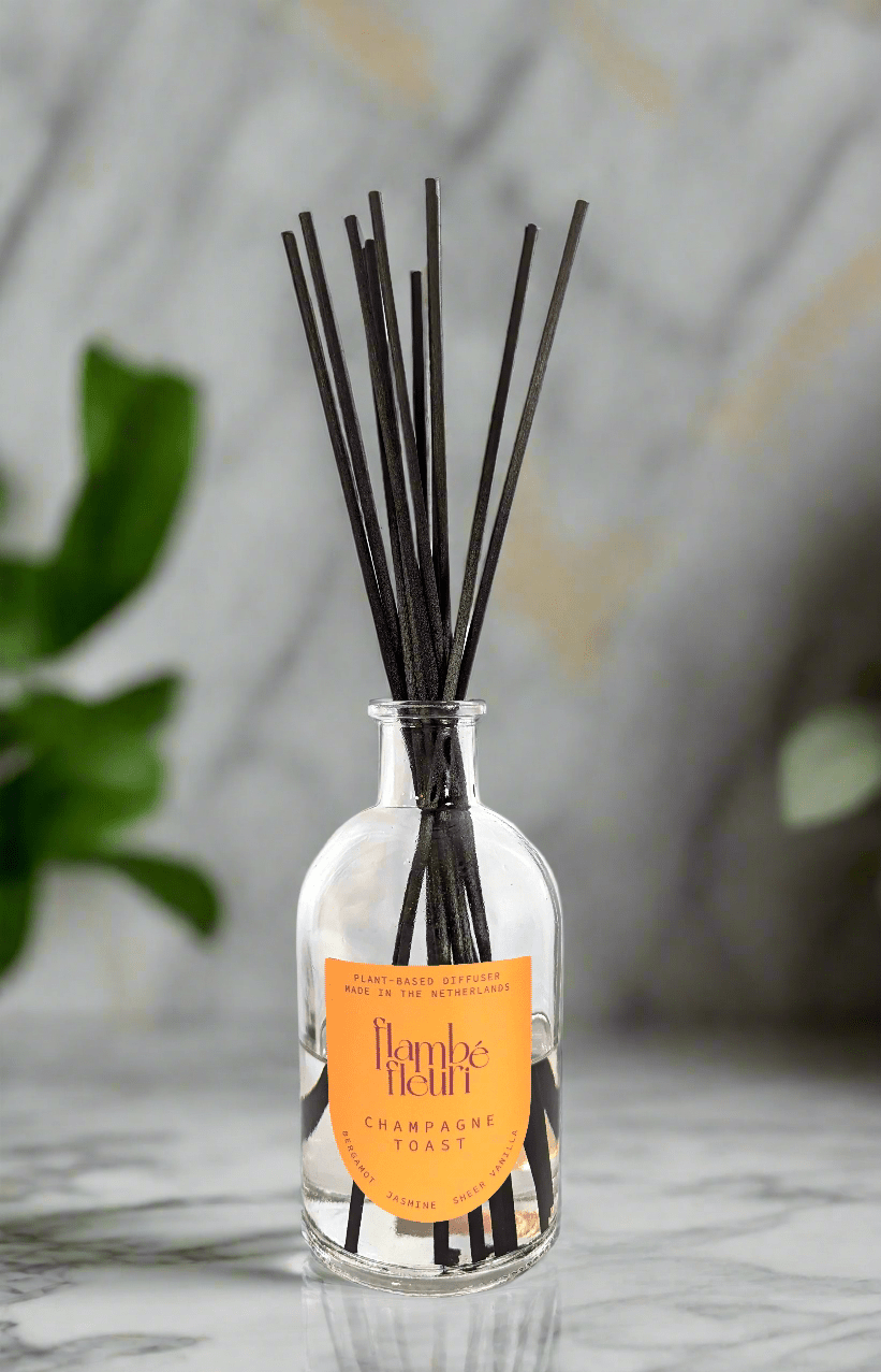 Non Toxic Reed diffuser with black fiber sticks in a glass bottle labeled 'Flambé Fleuri' on a marble surface.