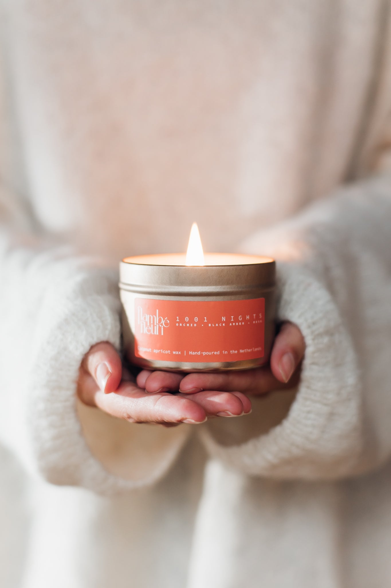Vegan Scented Candle - Oriental 1001 Nights - Non Toxic. Person holding a lit candle in a tin container with a visible brand label.
