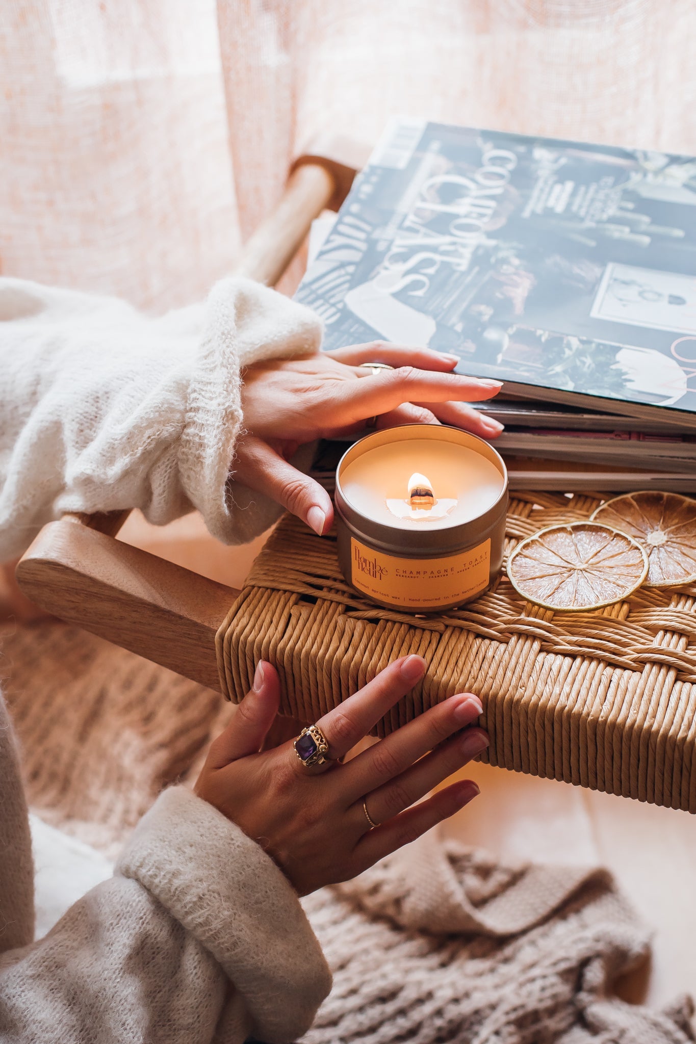 Person holding a lit vegan non toxic candle next to a book on a wooden surface with a soft, warm background.