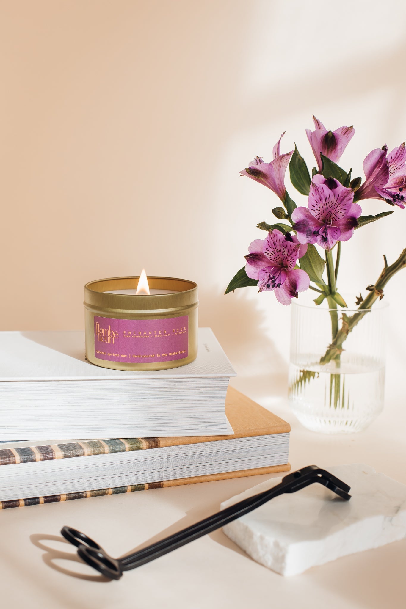 Non Toxic Vegan Candle with a purple label on books next to a vase of purple flowers on a light background